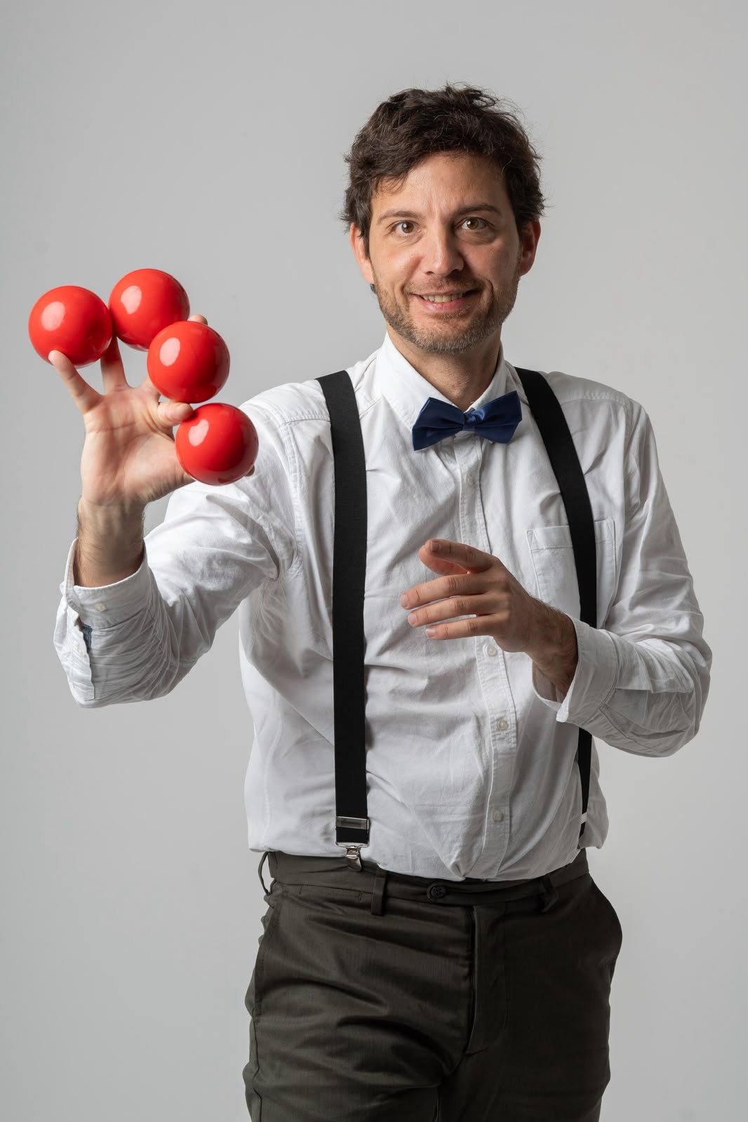 El mago Alexku, de camisa blanca y pajarita, sosteniendo en equilibrio cuatro bolas rojas sobre la mano