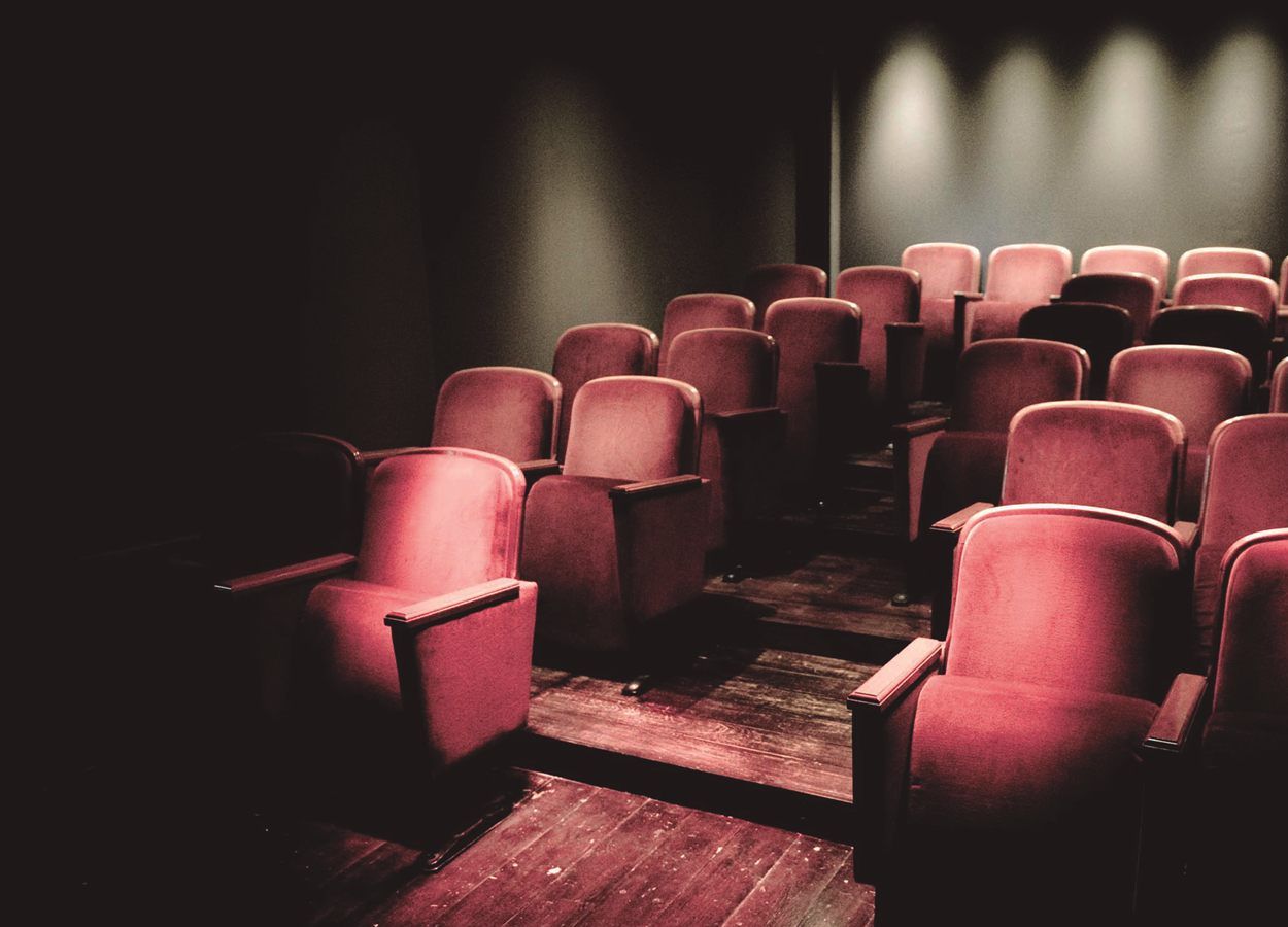 The red seats of CasaLa's auditorium, empty and in half-light under three stage lights