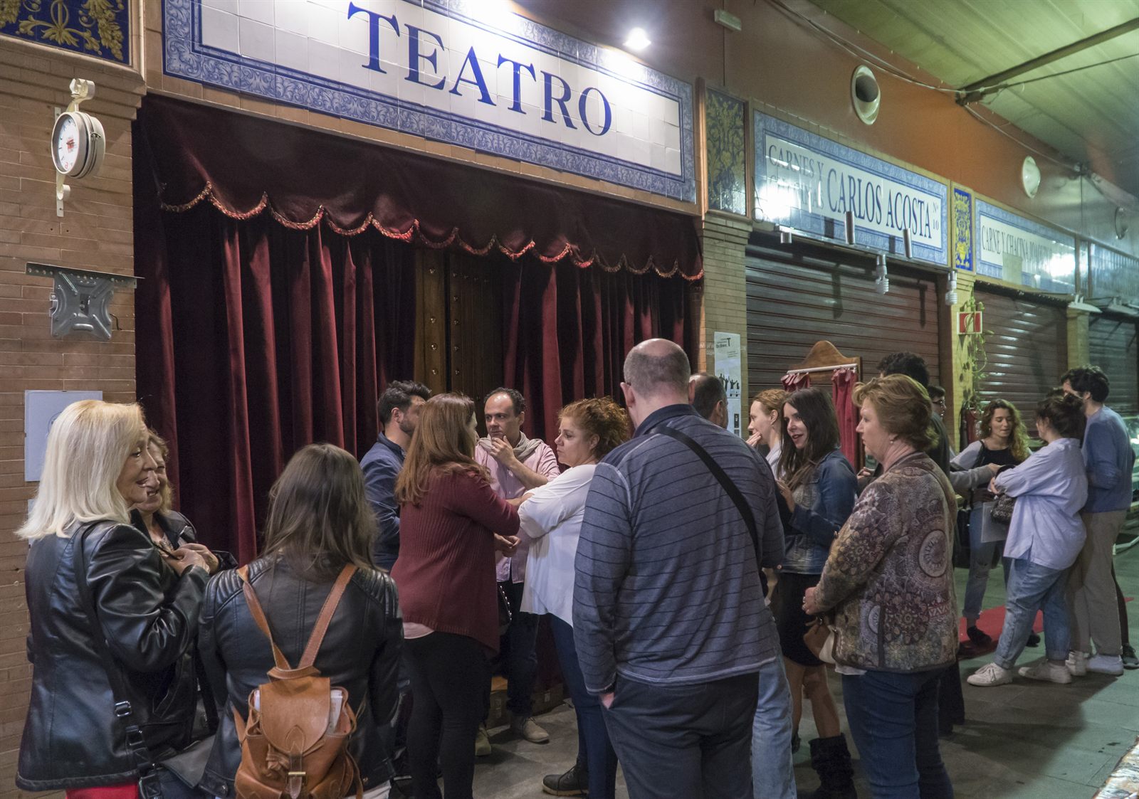 Público esperando a entrar en CasaLa Teatro, bajo el rótulo de azulejos que dice Teatro, entre los puestos cerrados del Mercado de Triana