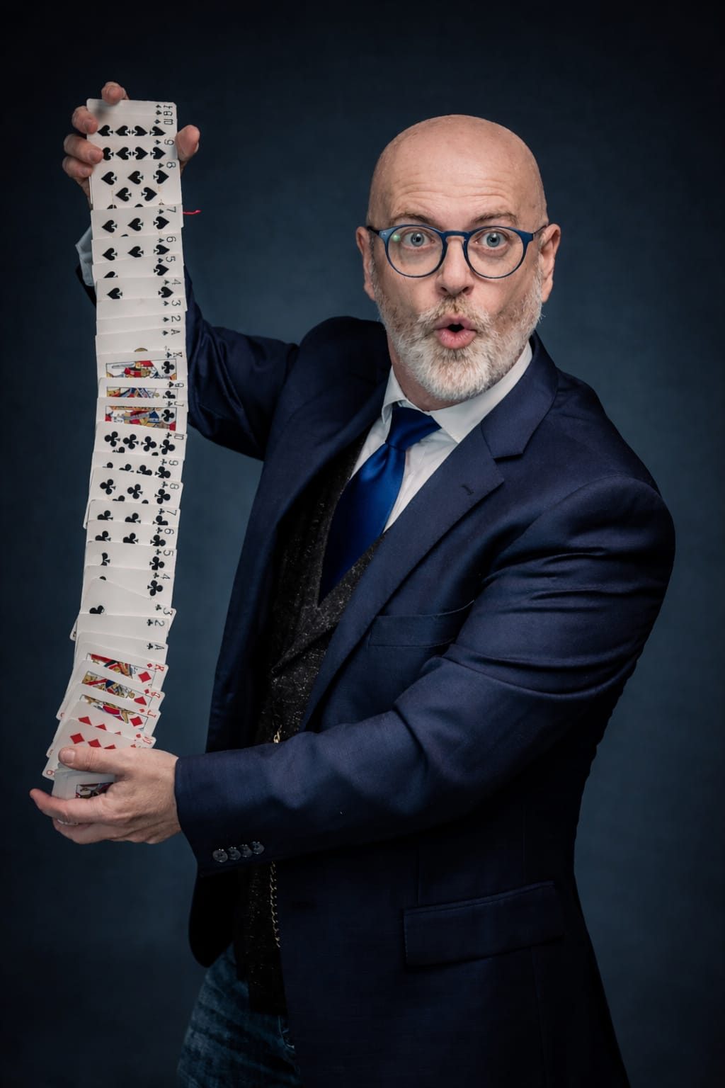 Magic Peter, de traje azul y gafas, sosteniendo con las dos manos una baraja desplegada en columna