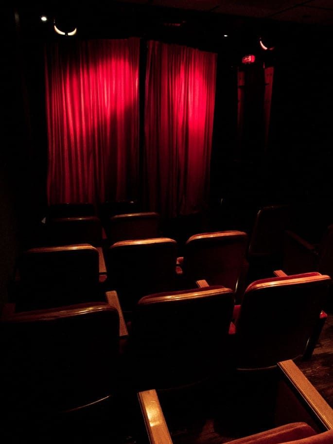 El telón rojo del escenario encendido por un foco, visto desde las últimas butacas de la sala en penumbra